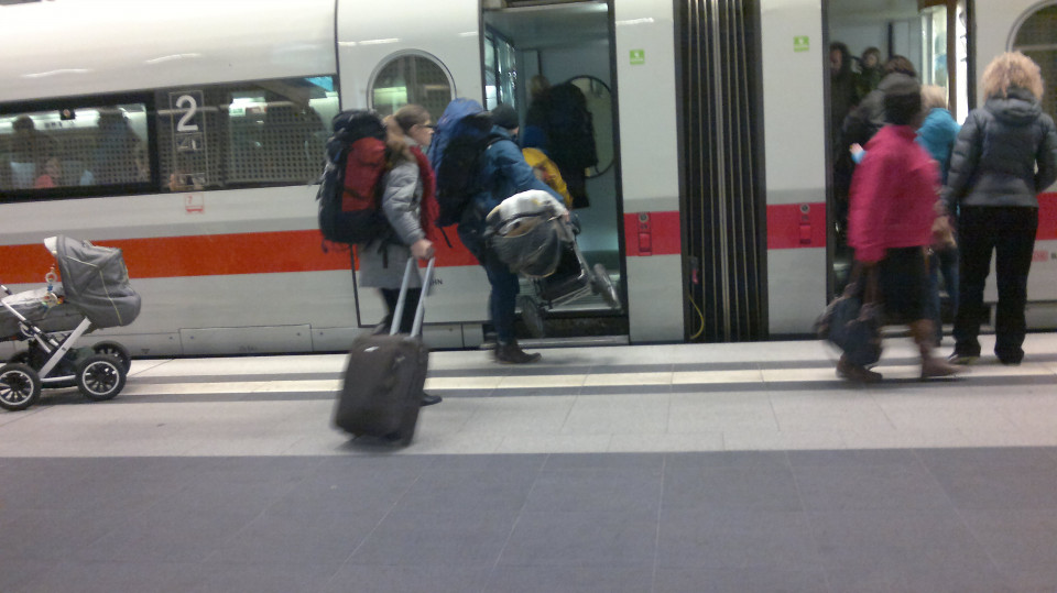 Eine Person hieft einen Kinderwagen in einen ICE, der am Bahnsteig steht.