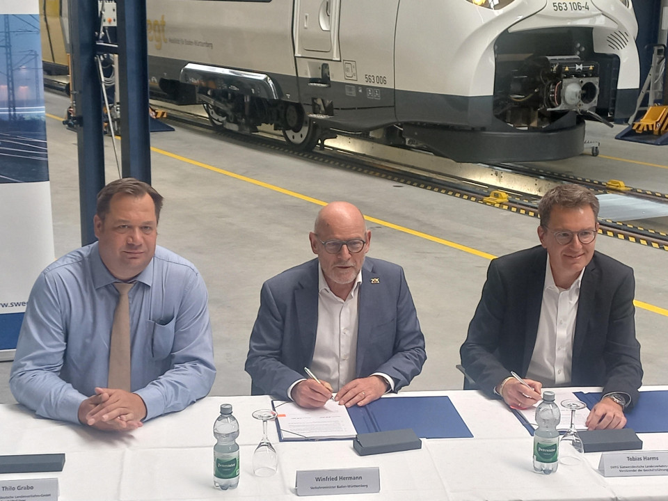 An einem Tisch in der Fahrzeughalle sitzen zur Vertragsunterzeichnung des neuen Verkehrsvertrages Landesverkehrsminister Winfried Herrmann und SWEG-Geschäftsführer Tobias Harms