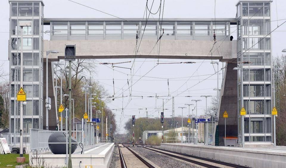 Zwei Seitenbahnsteige mit je einem Gleis und Aufzugstürmen an einer elektrifizierten Eisenbahnstrecke.