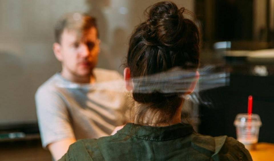 Zwei Menschen sitzen an einem Tisch gegenüber. Der vordere Mensch ist mit dem Rücken zu sehen.