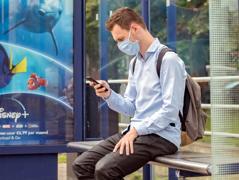 Eine Person wartet an einer Bushaltestelle mit Maske auf einen Bus.
