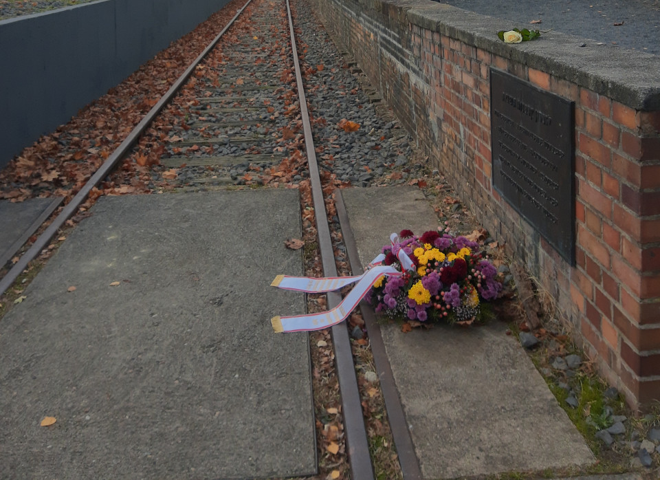 Ein verrostetes Gleis im Güterbahnhof Grunewald. Links und rechts Rampen, rechts an derSeite eine Gedenktafel mit einem davor liegenden Blumenkranz