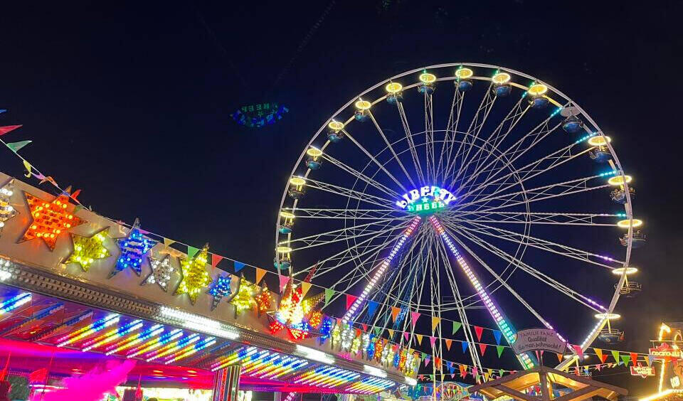 Beleuchtetes Riesenrad bei Nacht auf dem Prämienmarkt mit bunten Lichterketten und Wimpelgirlanden