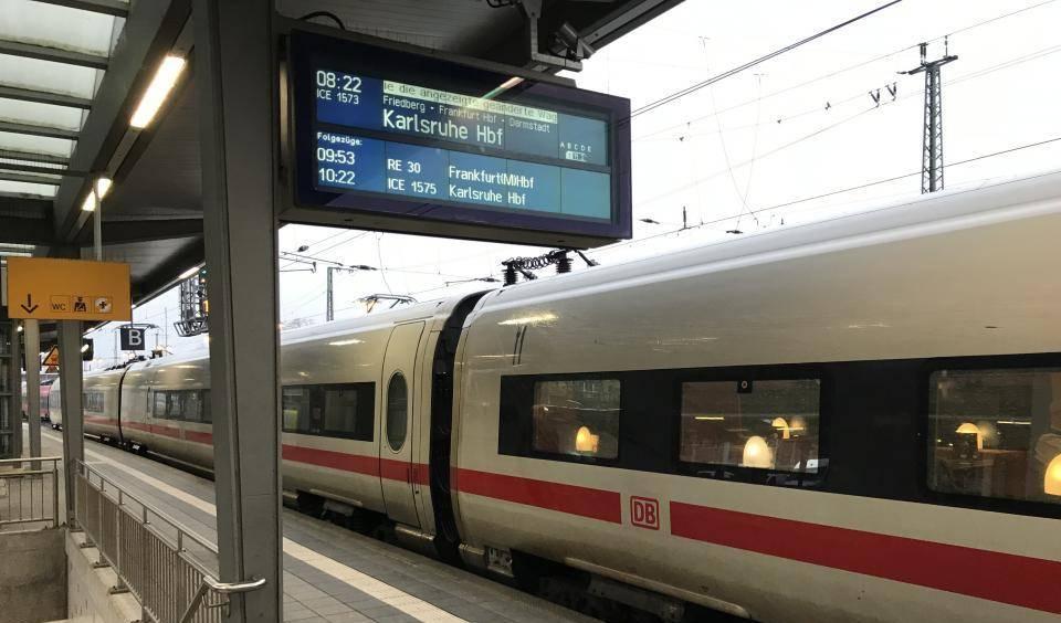 ICE-Zug mit DB-Logo steht am Bahnsteig in Gießen, darüber digitale Anzeigetafel mit Abfahrtszeiten und Ziel Karlsruhe Hbf.
