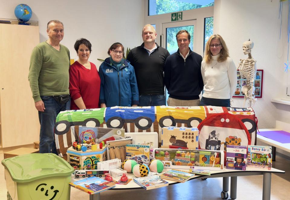 Mitglieder des Vorstandes der Lumdatalbahn und des Kindergartens bei der Geschenkeübergabe. Sie stehen hinter einem Tisch mit bunten Spielzeugen und Geschenke
