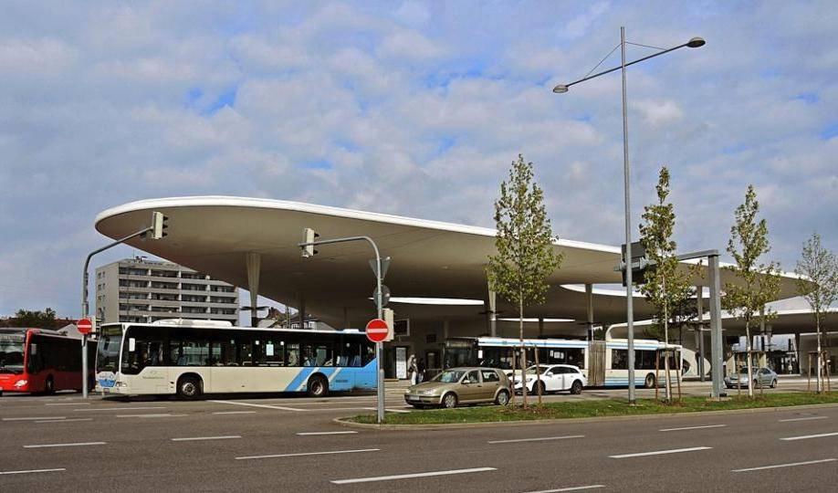 Busbahnhof Pforzheim mit mehreren Bussen unter einem großen, geschwungenen Dach und einigen Bäumen davor.