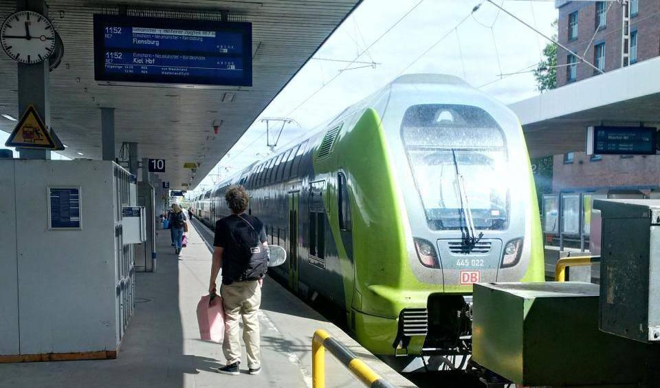 Bahnhof Altona, grüner Doppelstockzug nach Kiel Hbf der DB am Bahnsteig 10 mit einem Reisenden, der den Bahnsteig entlanggeht und digitaler Anzeigetafel.
