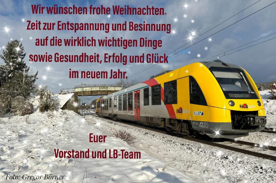 Gelber Regionalzug auf schneebedecktem Gleis vor verschneiten Bäumen und Brücke, darüber roter Weihnachtsgrußtext.
